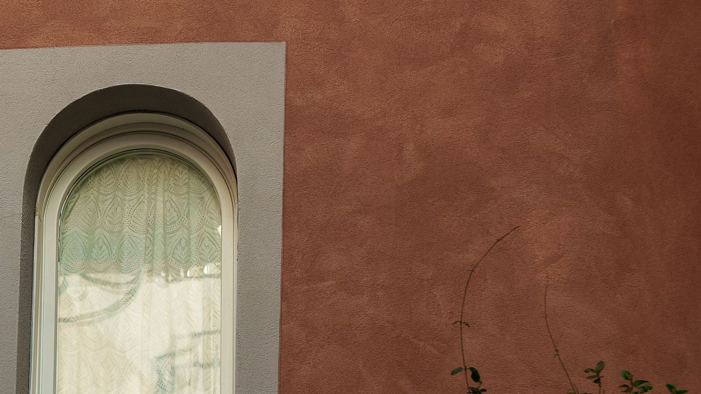 Arched window against a textured reddish-brown wall.