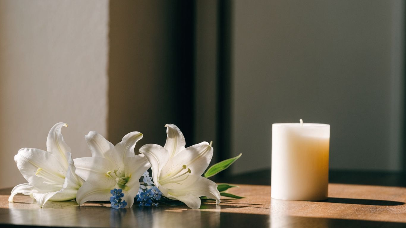 Soft white and blue flowers arranged beside a memorial candle
