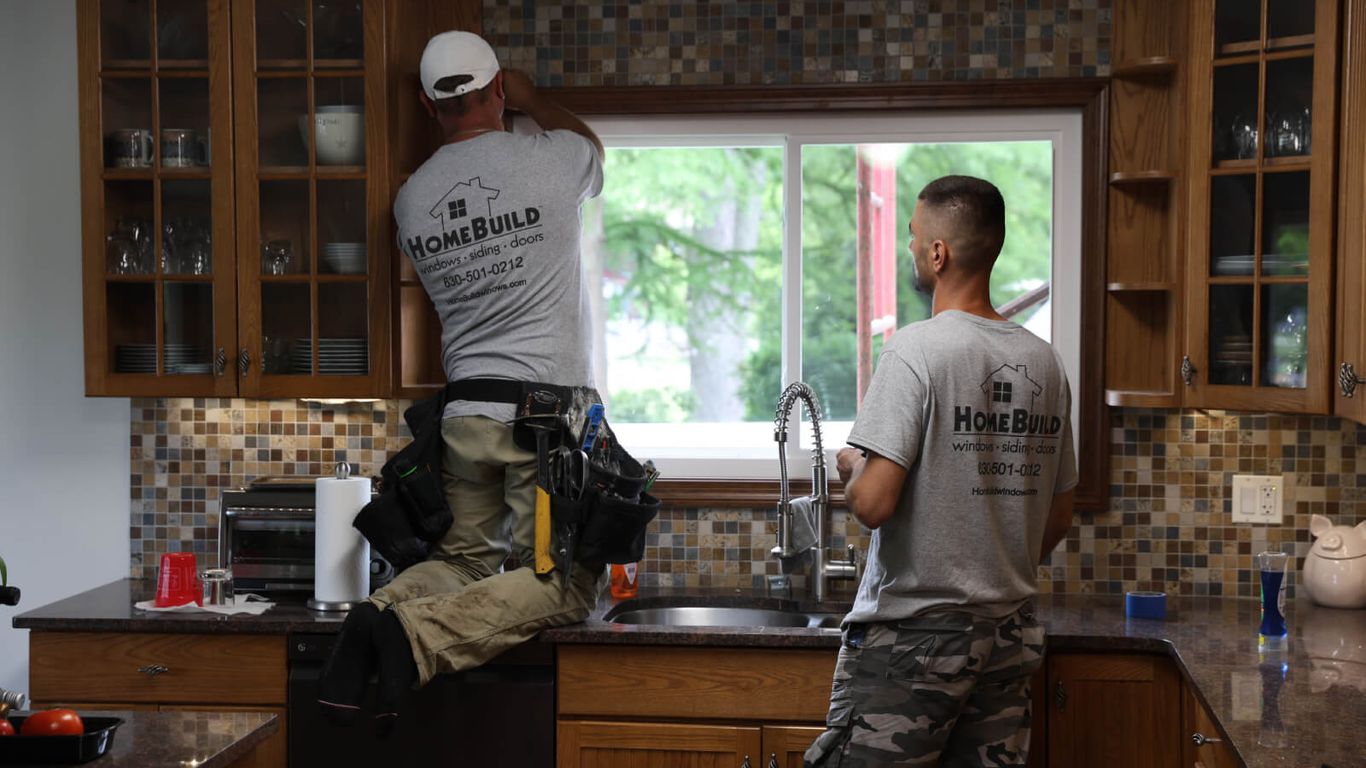 Two people installing a window in a kitchen.