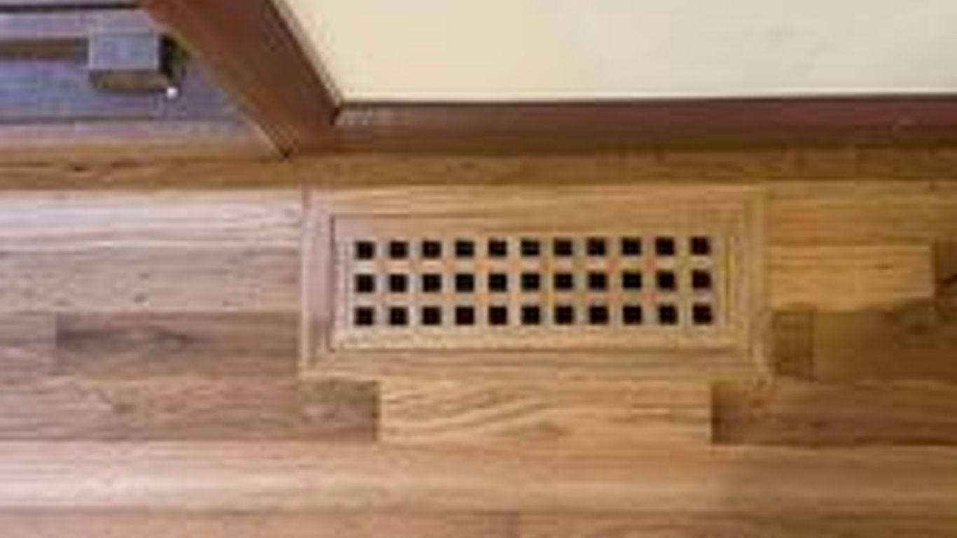 A wooden floor vent cover on hardwood flooring.