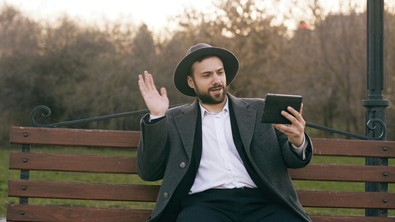 Man in hat waves at tablet on park bench