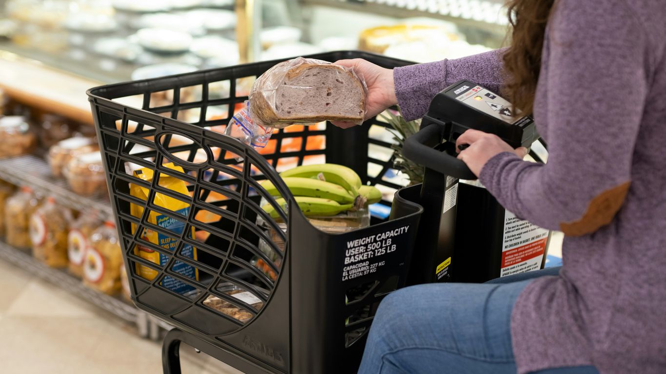 a woman sitting in a grocery cart with a sandwich in her hand