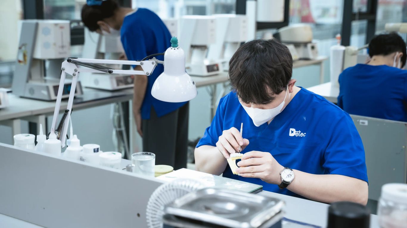 People in blue shirts working on dental prosthetics in a lab.