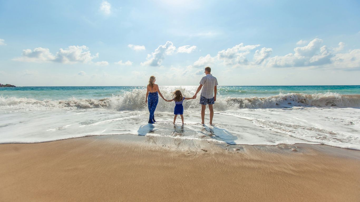 man, woman and child holding hands on seashore