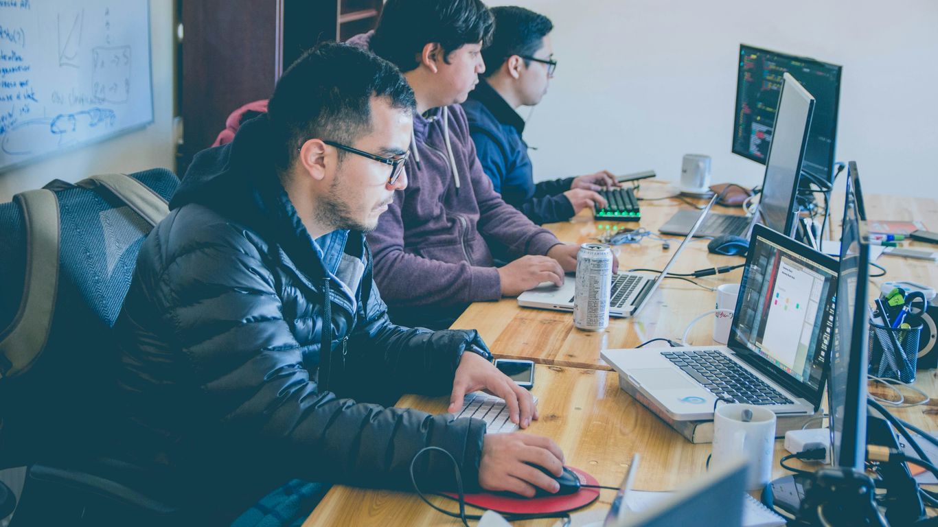 three men facing computer monitors