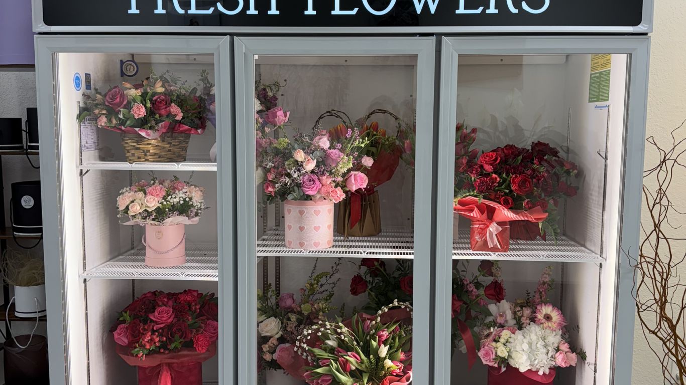A refrigerated display case filled with various fresh flower arrangements.
