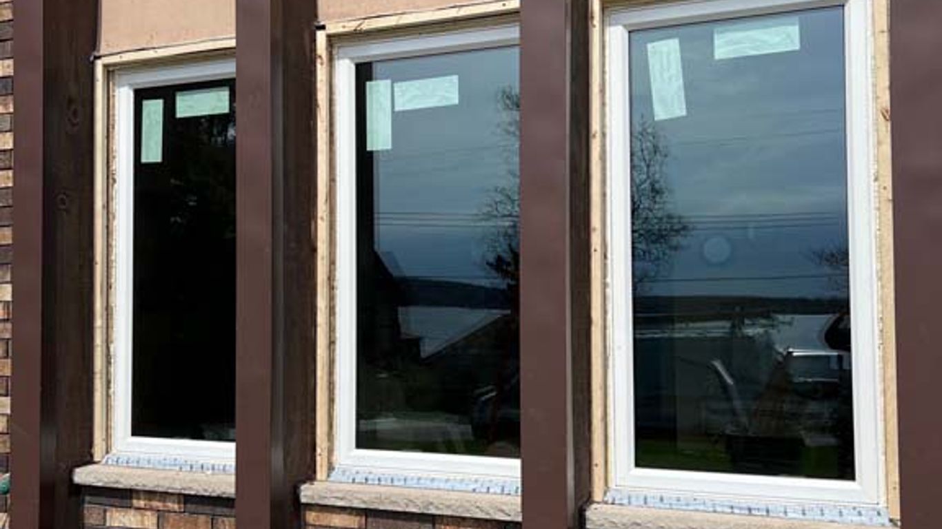 Three new windows are installed on a brick house exterior.