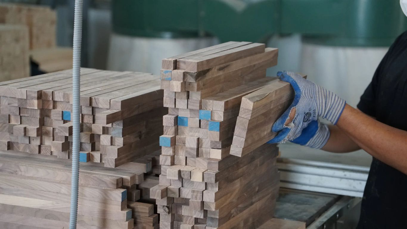 A person in gloves stacks lumber in a workshop.