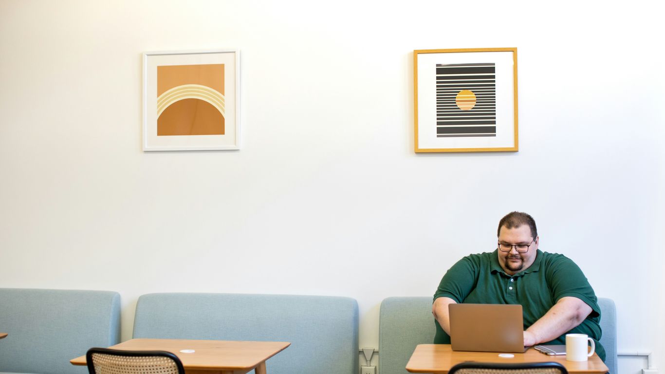 man in green polo shirt sitting on sofa near table while using laptop computer inside room