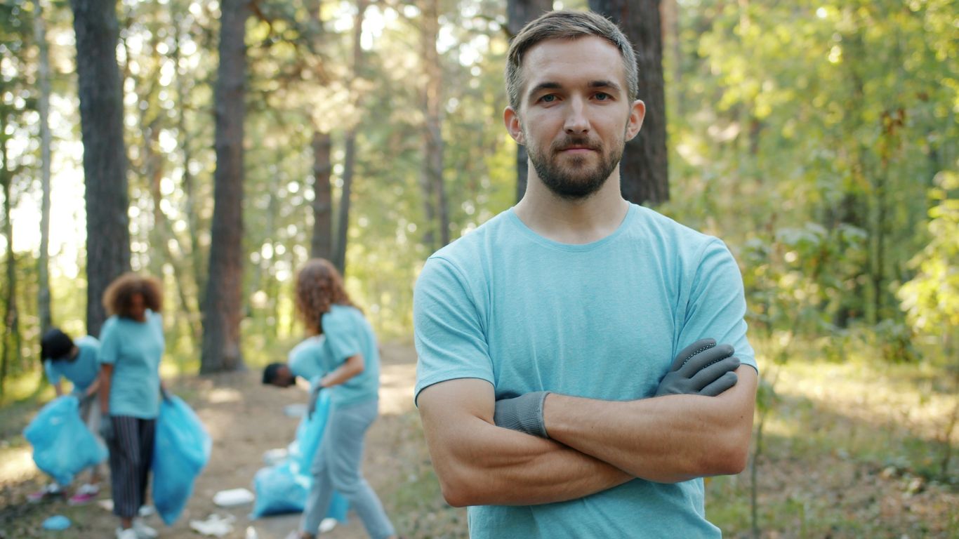 Man with arms crossed in a forest cleanup.