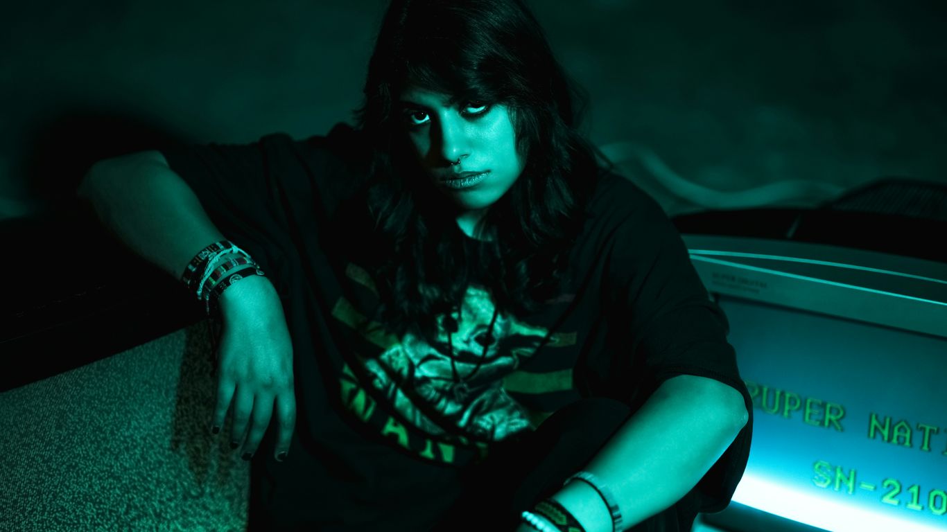 Young person with dark hair and bracelets sits.