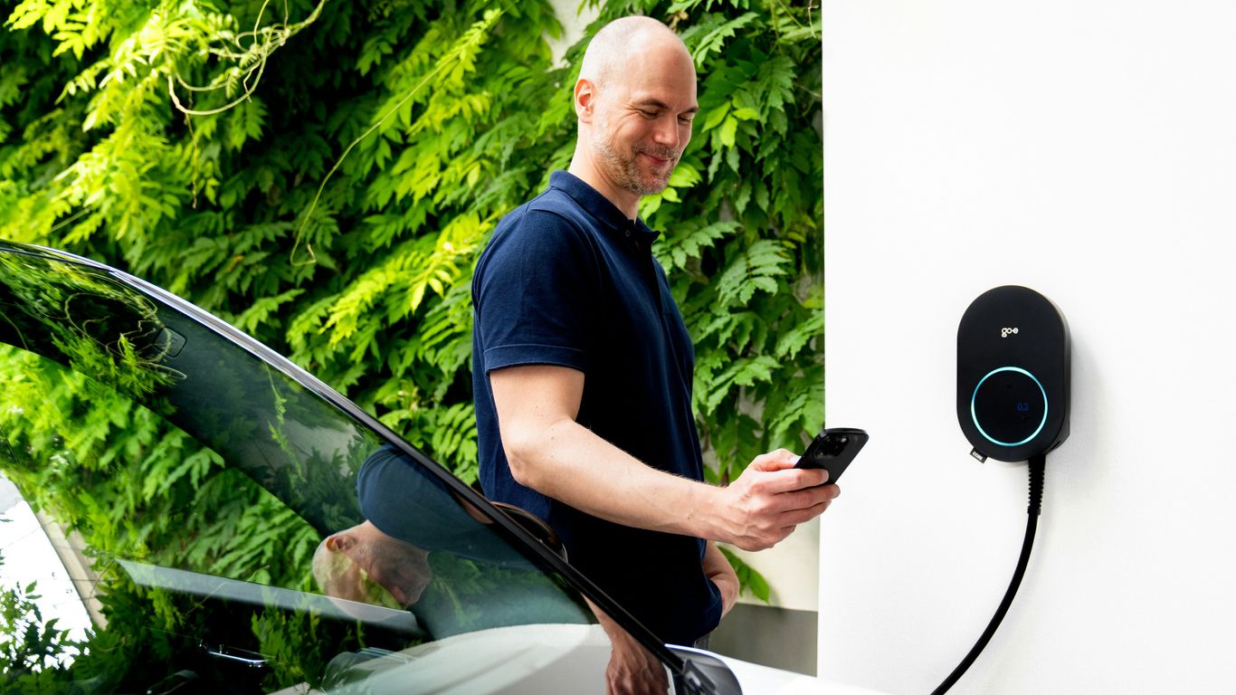 Man using phone near electric car charging station.