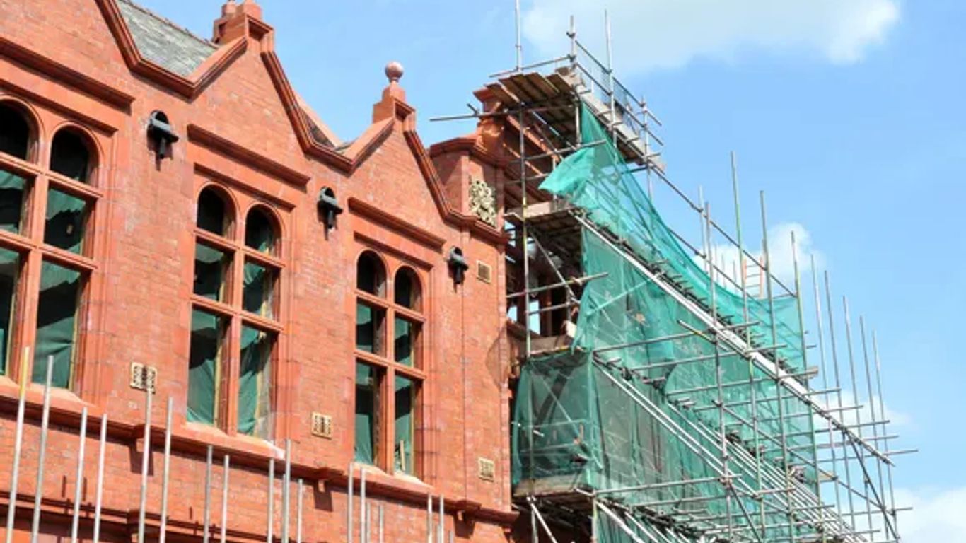 Red brick building undergoing renovation with scaffolding and green netting.
