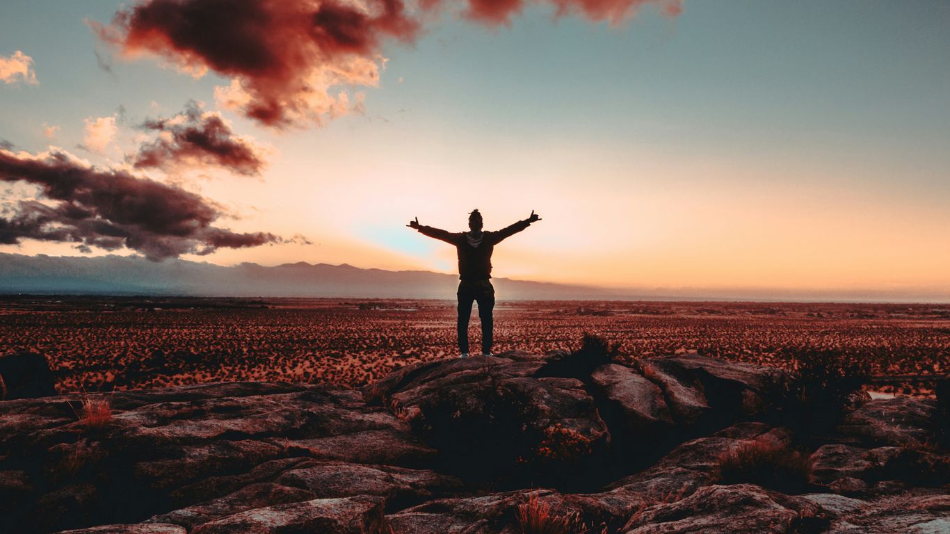person standing on rock raising both hands