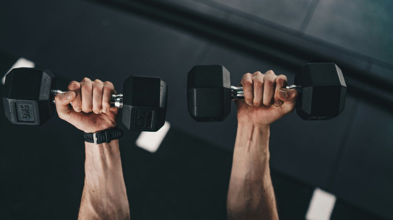 a man lifting two dumbs in a gym