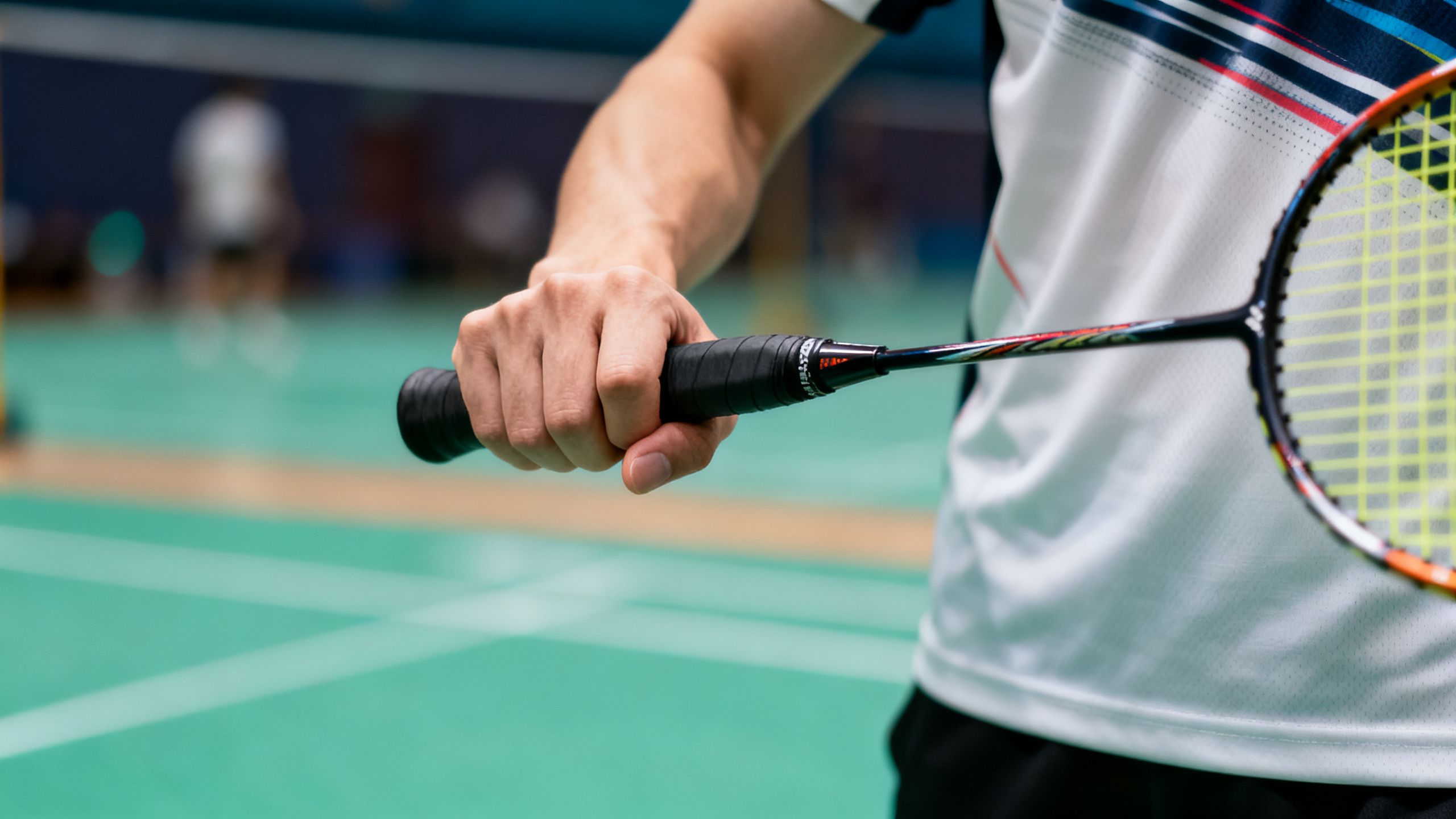 Badminton player using backhand thumb grip on racket handle.