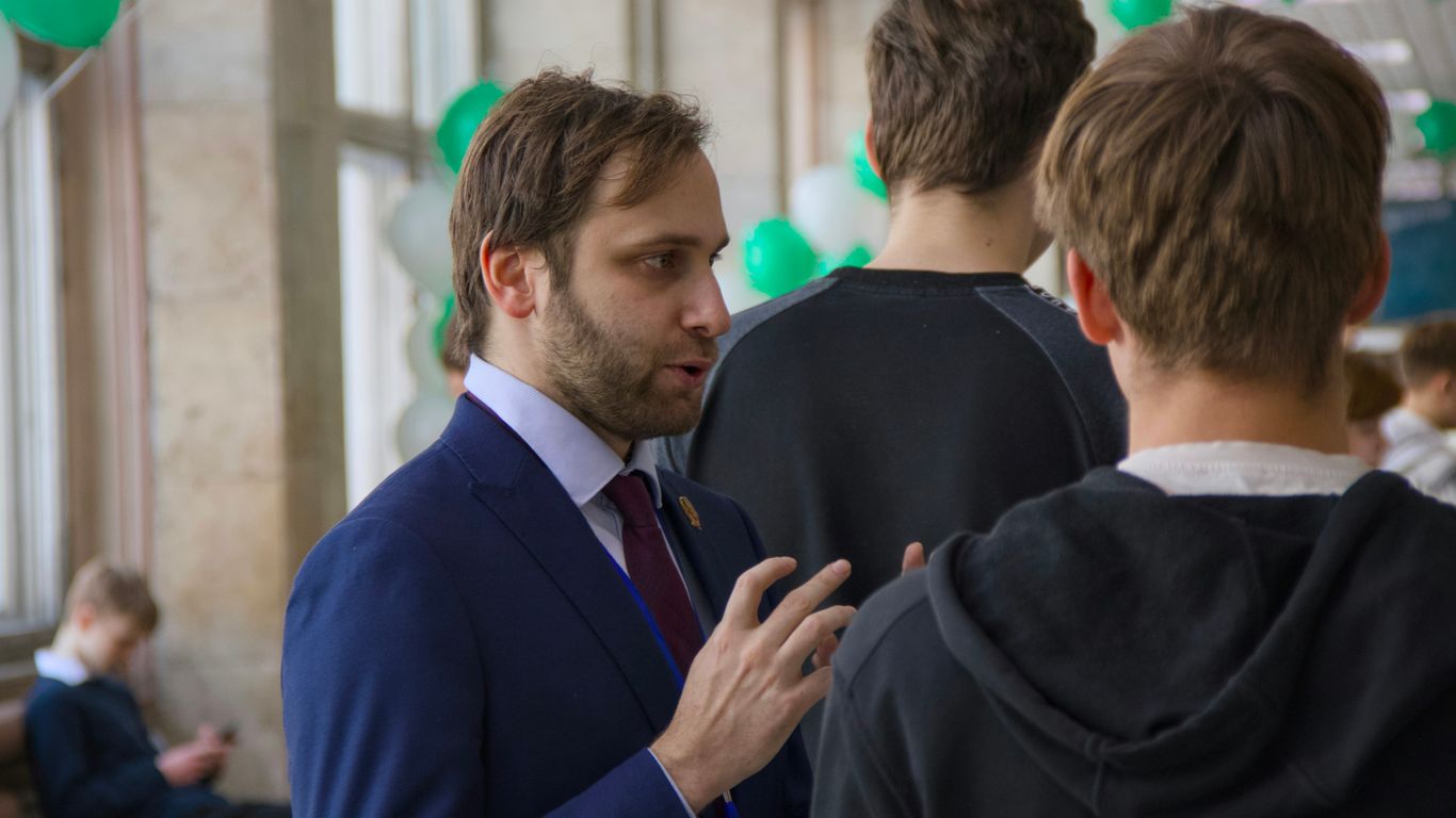 A man in a suit talks to two young men.