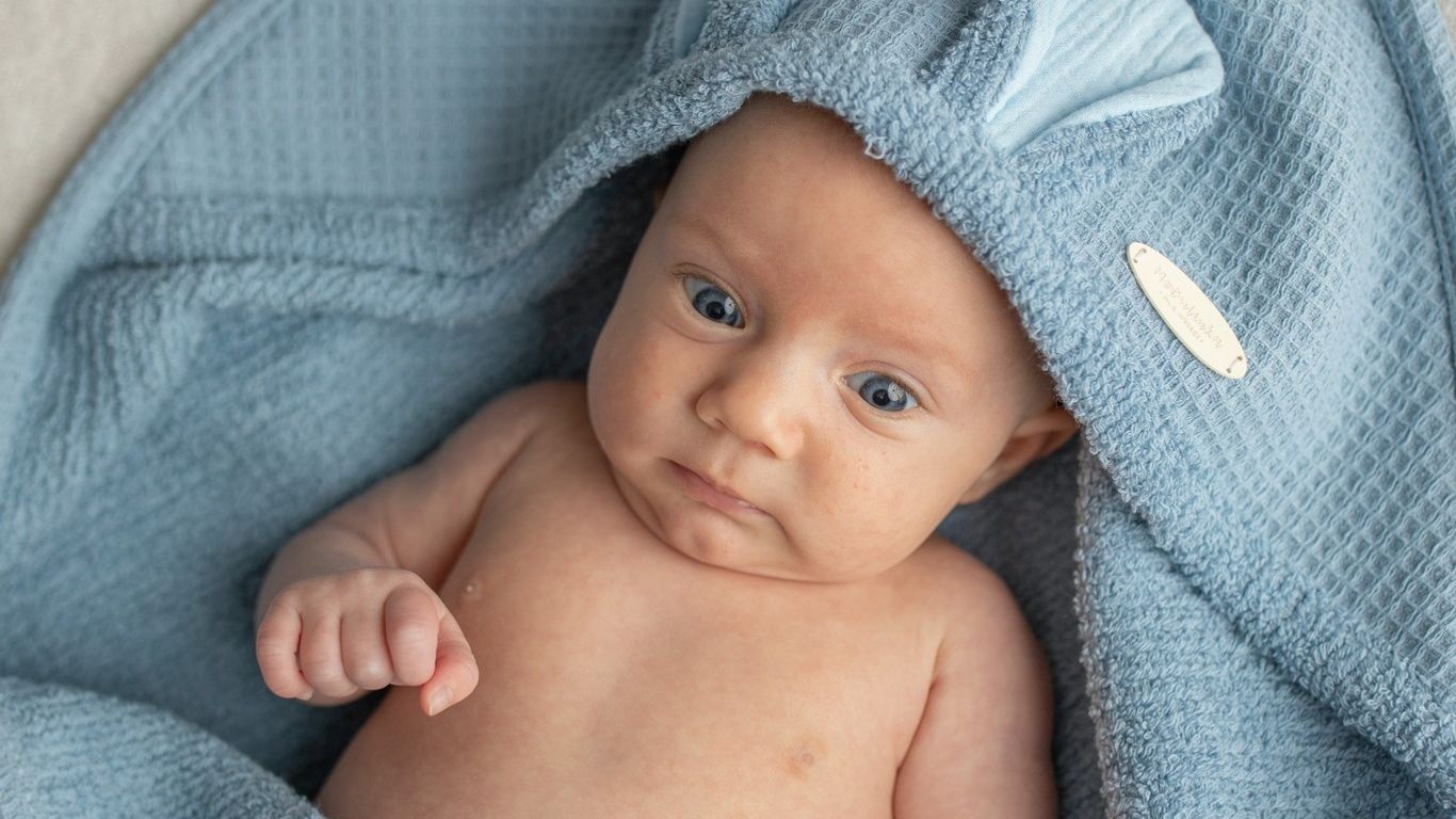 A baby wrapped in a blue hooded towel with bunny ears.
