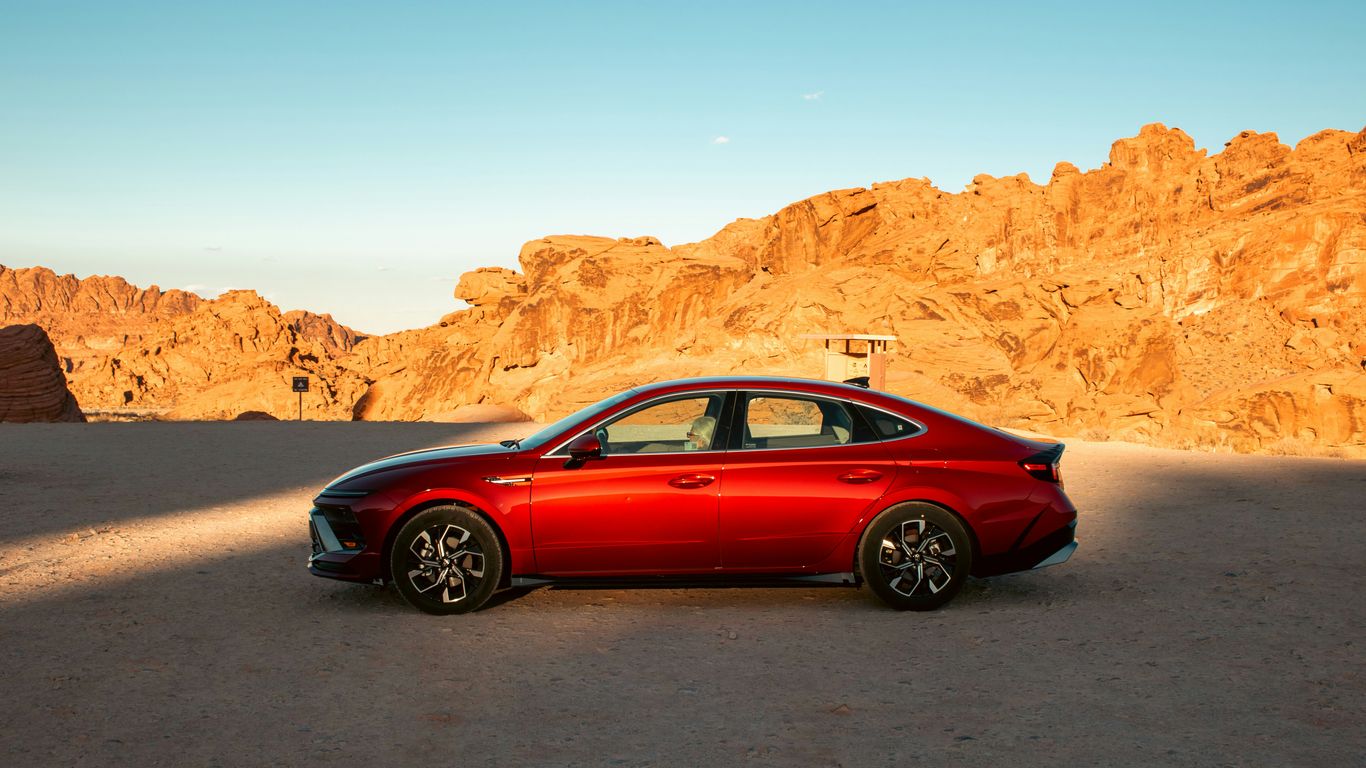 A red car is parked in a desert landscape.