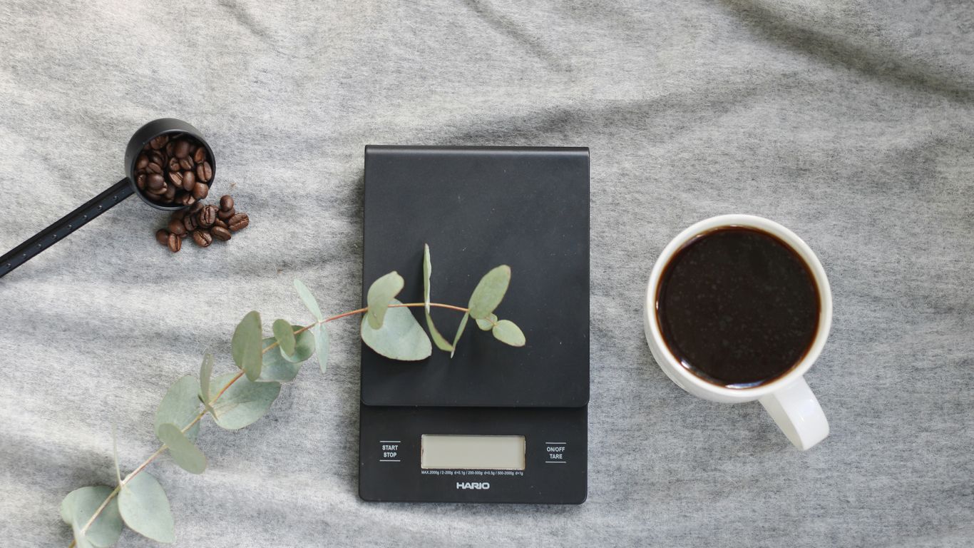 a scale, a cup of coffee and a spoon on a bed