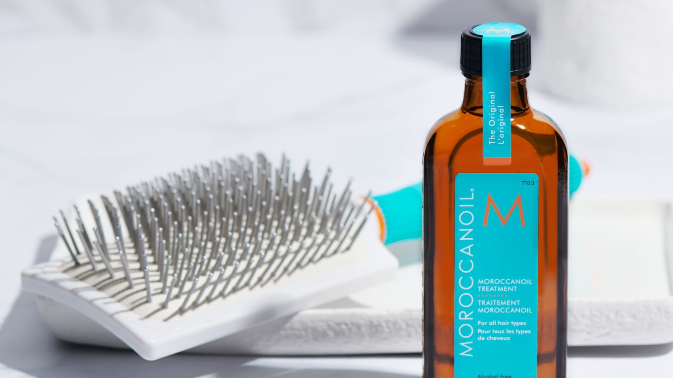 Moroccanoil hair treatment bottle next to a hairbrush on marble.