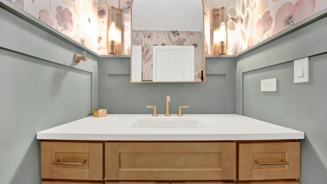 A modern bathroom vanity with floral wallpaper and brass fixtures.