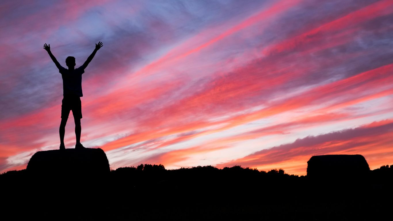silhouette of man standing on high ground under red and blue skies