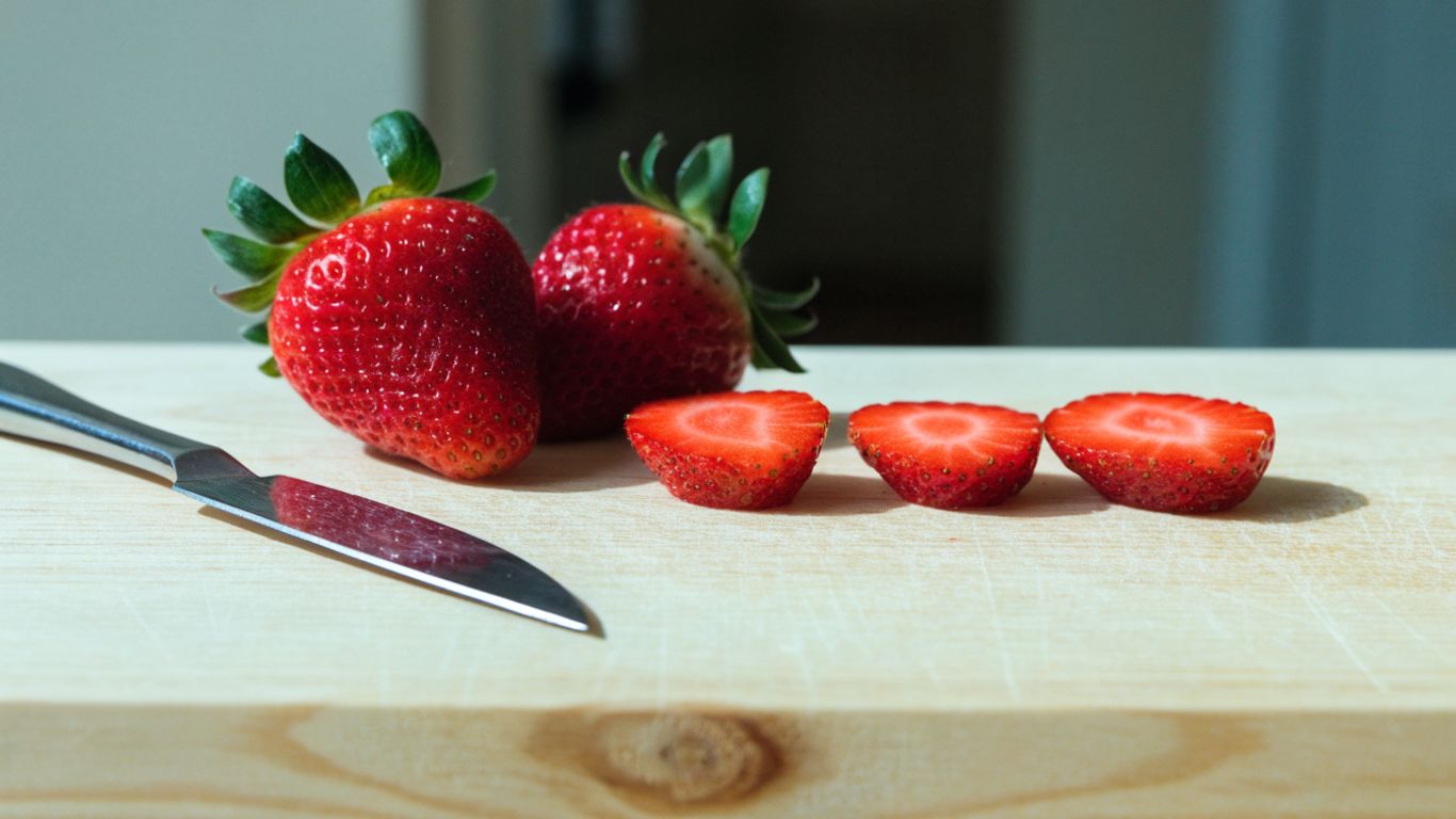 Even strawberry slices beside whole berries on a pale maple board