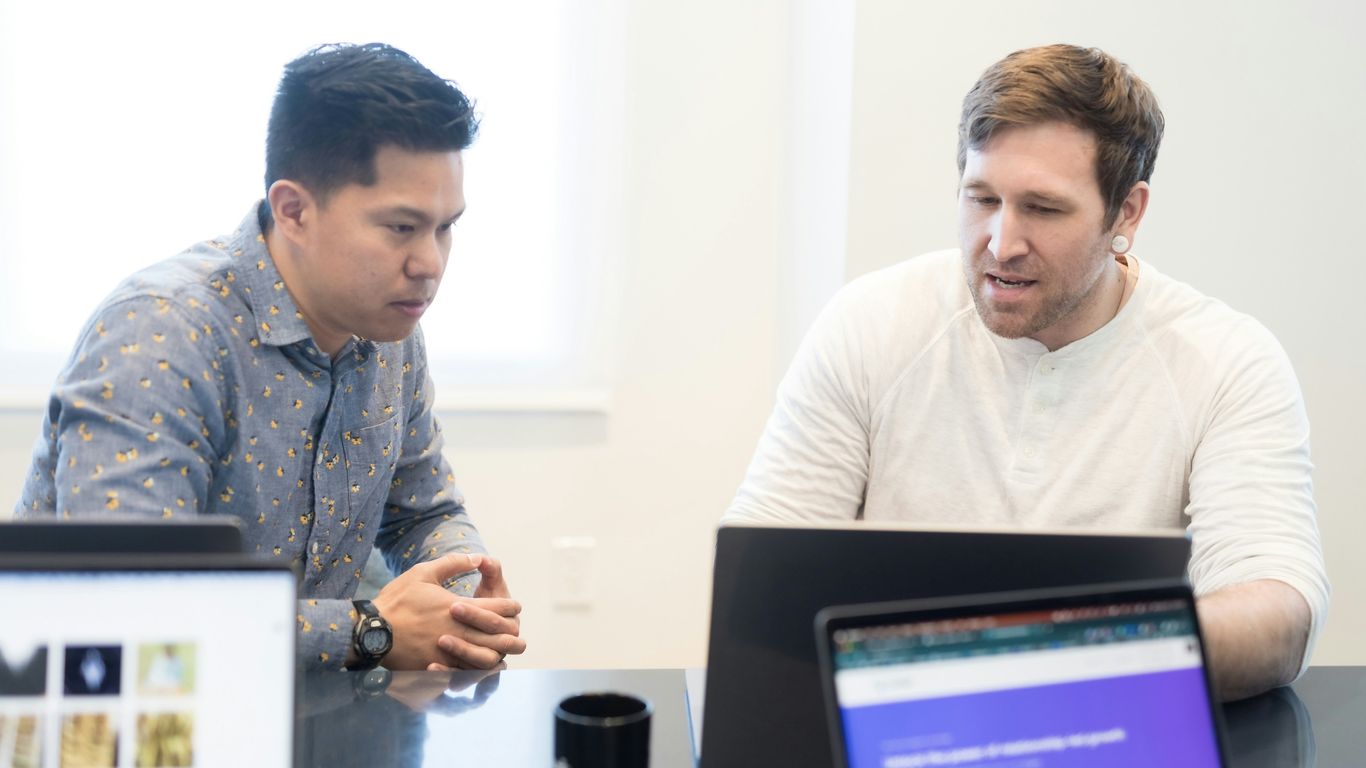 two men sitting at a table looking at a laptop