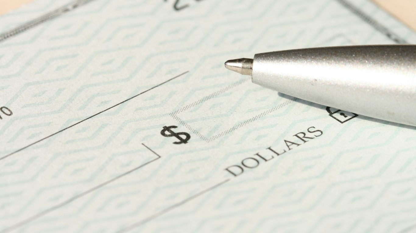 A pen rests on a check near the dollars line.