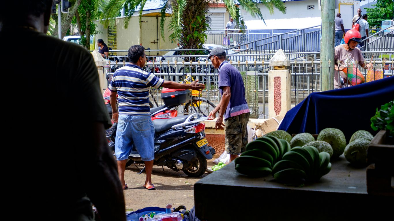 Men interacting at an outdoor market stall with produce.
