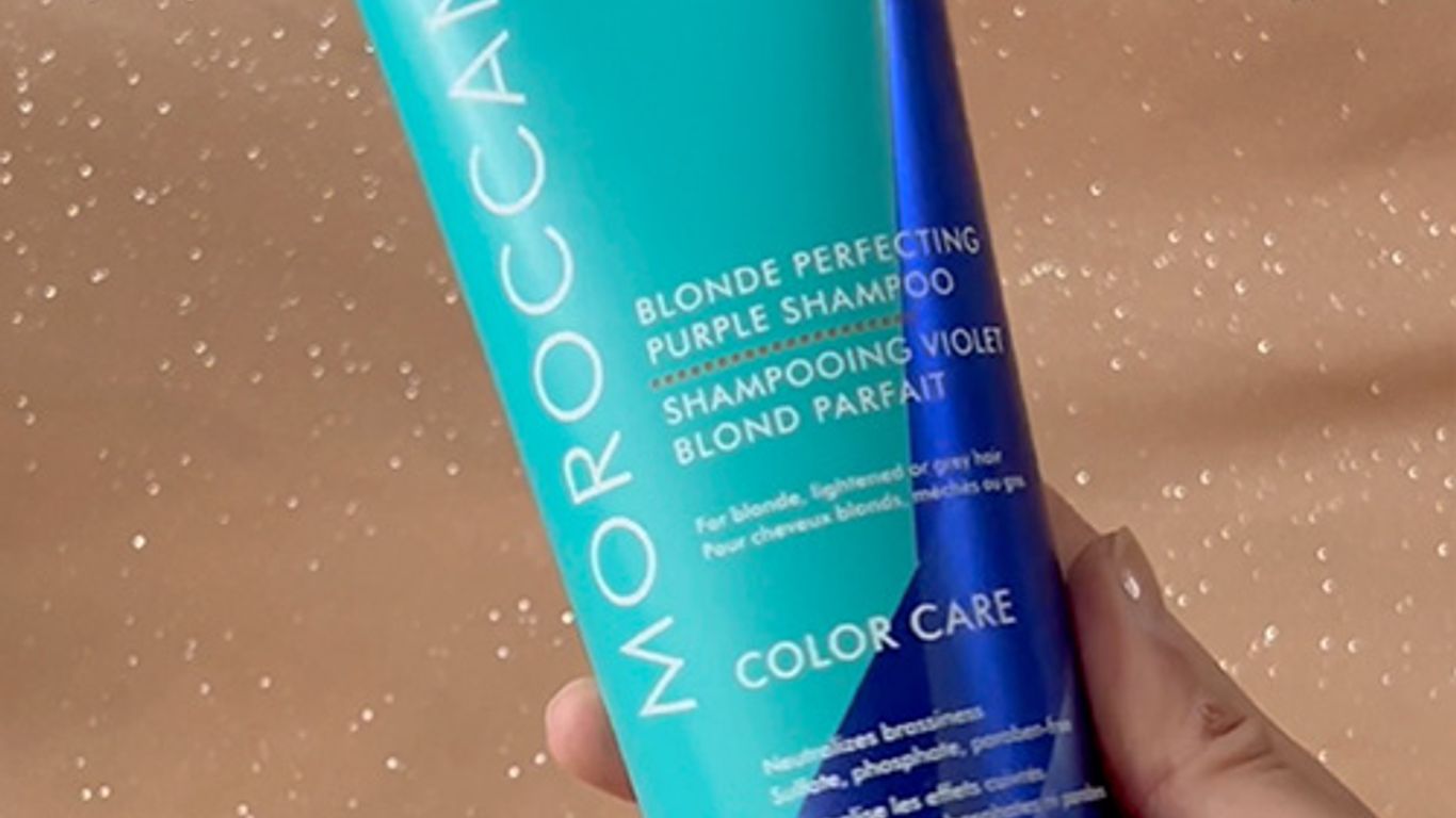 A hand holding a bottle of Moroccanoil purple shampoo.