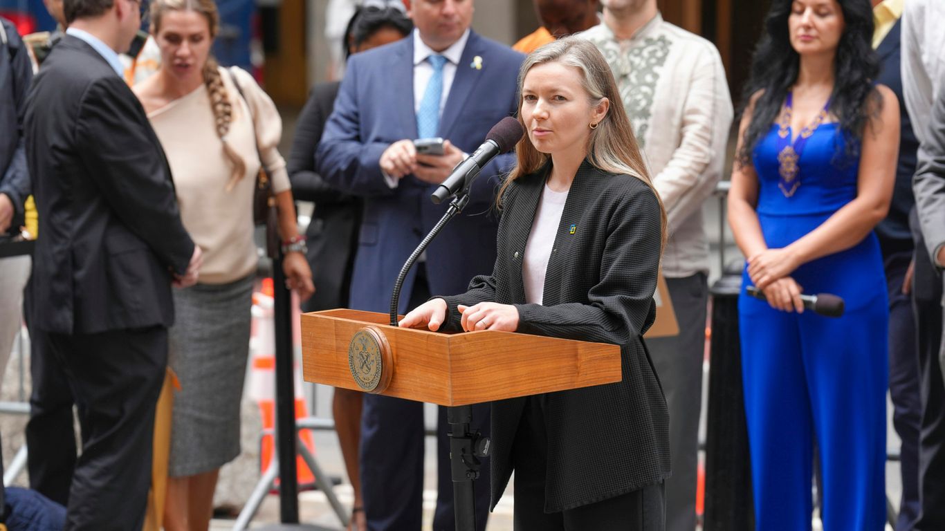 Woman speaks at podium with crowd behind her