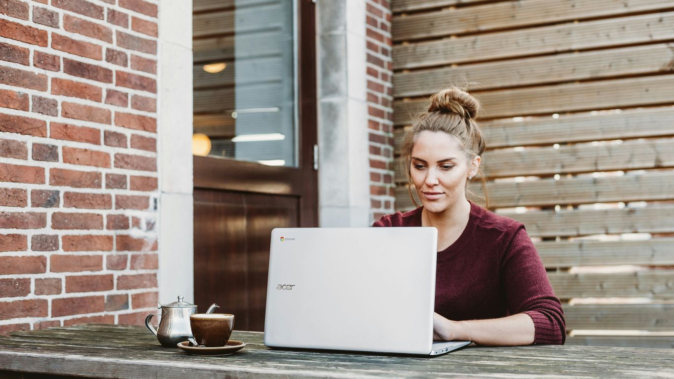 woman sitting and holding white Acer laptop near brown wooden wall