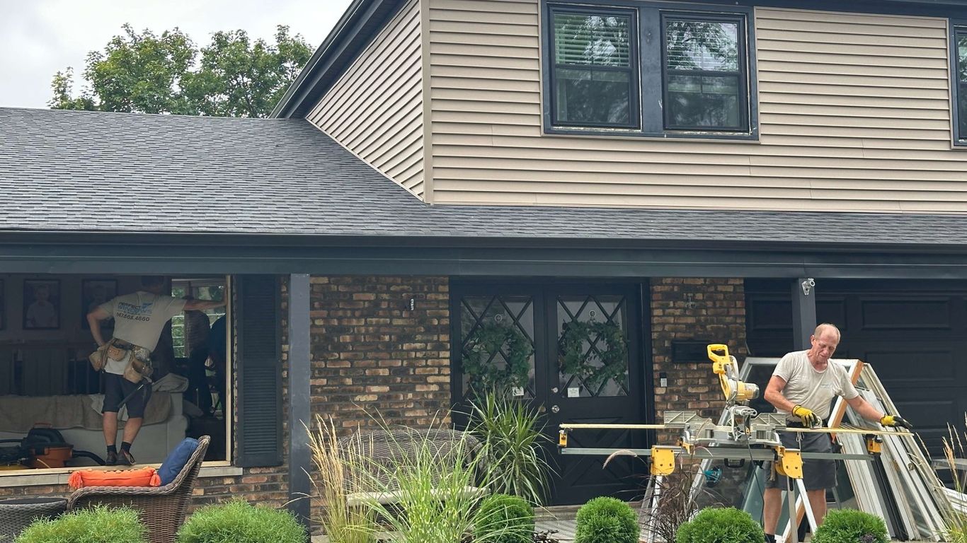 Workers installing new windows on a house exterior.