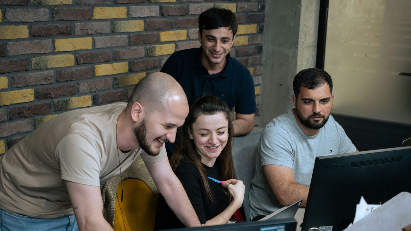 A group of people sitting around a laptop computer