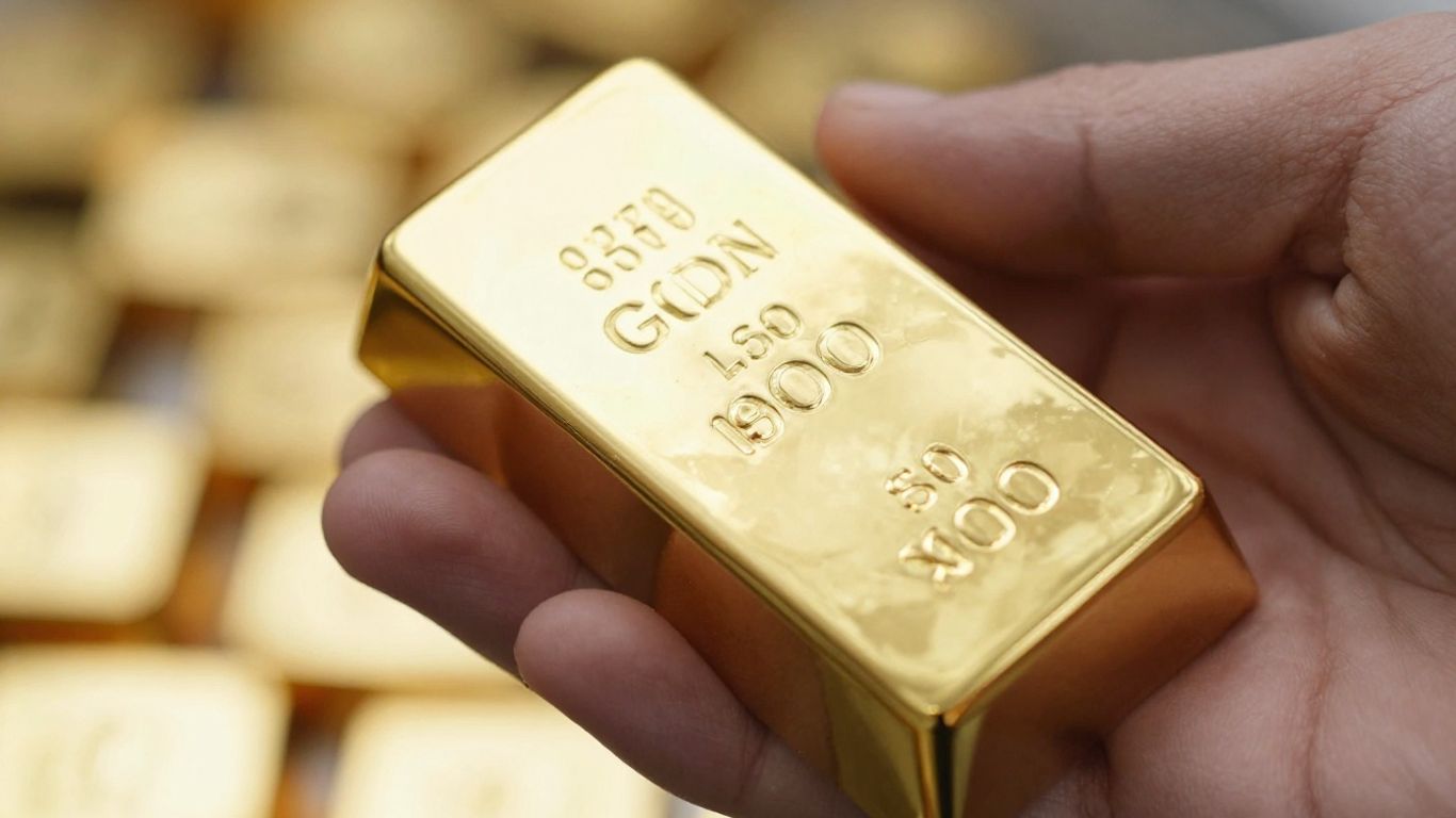 Main d'une personne tenant une barre d'or brillante.