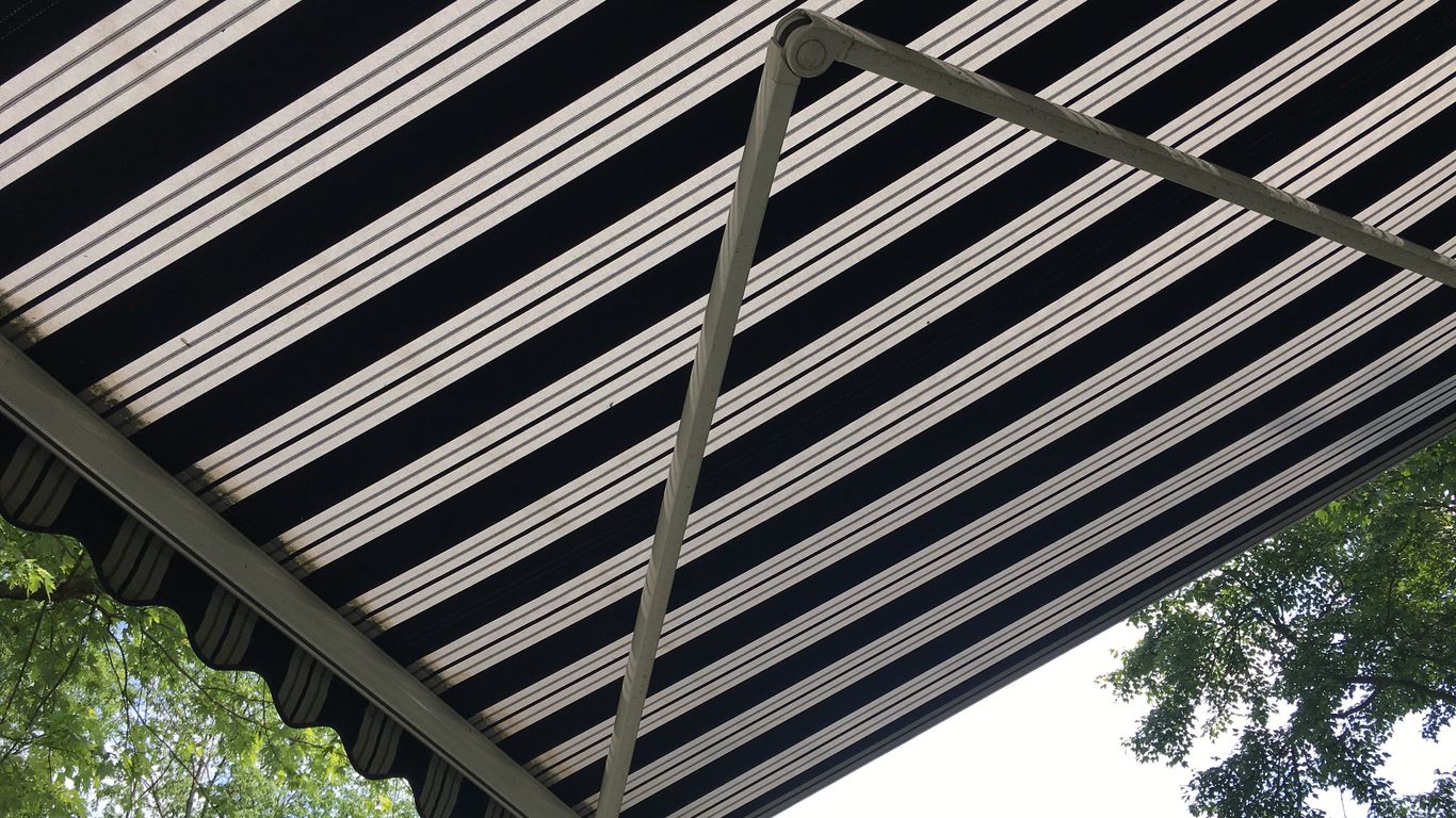 Black and white striped awning with metal frame against trees and sky.