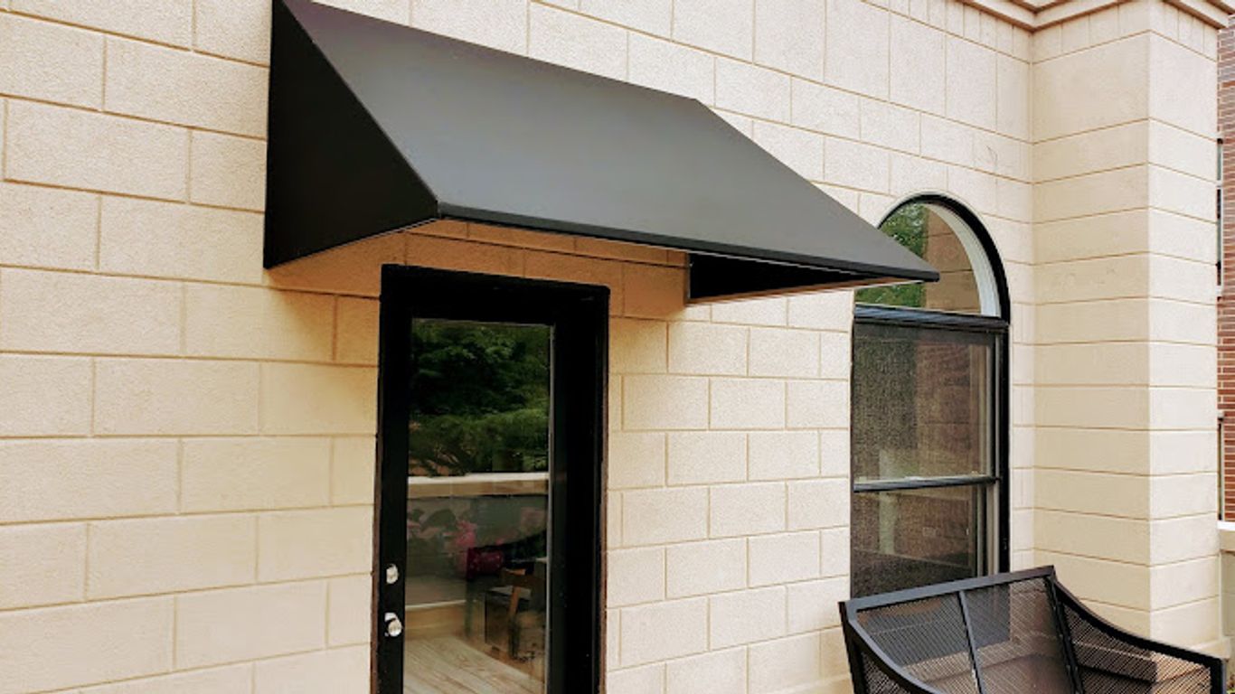 A black awning covers a door and window on a brick building.