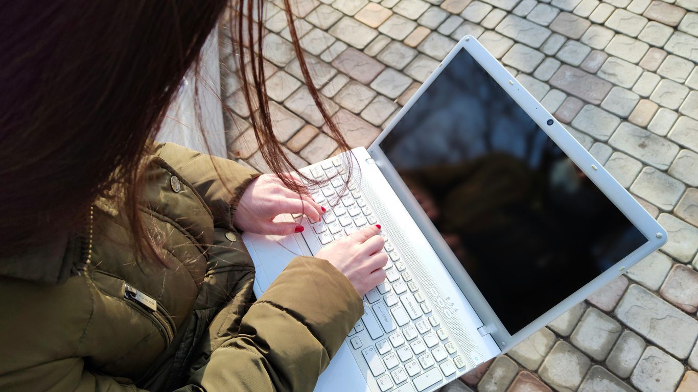 a woman is typing on her laptop outside