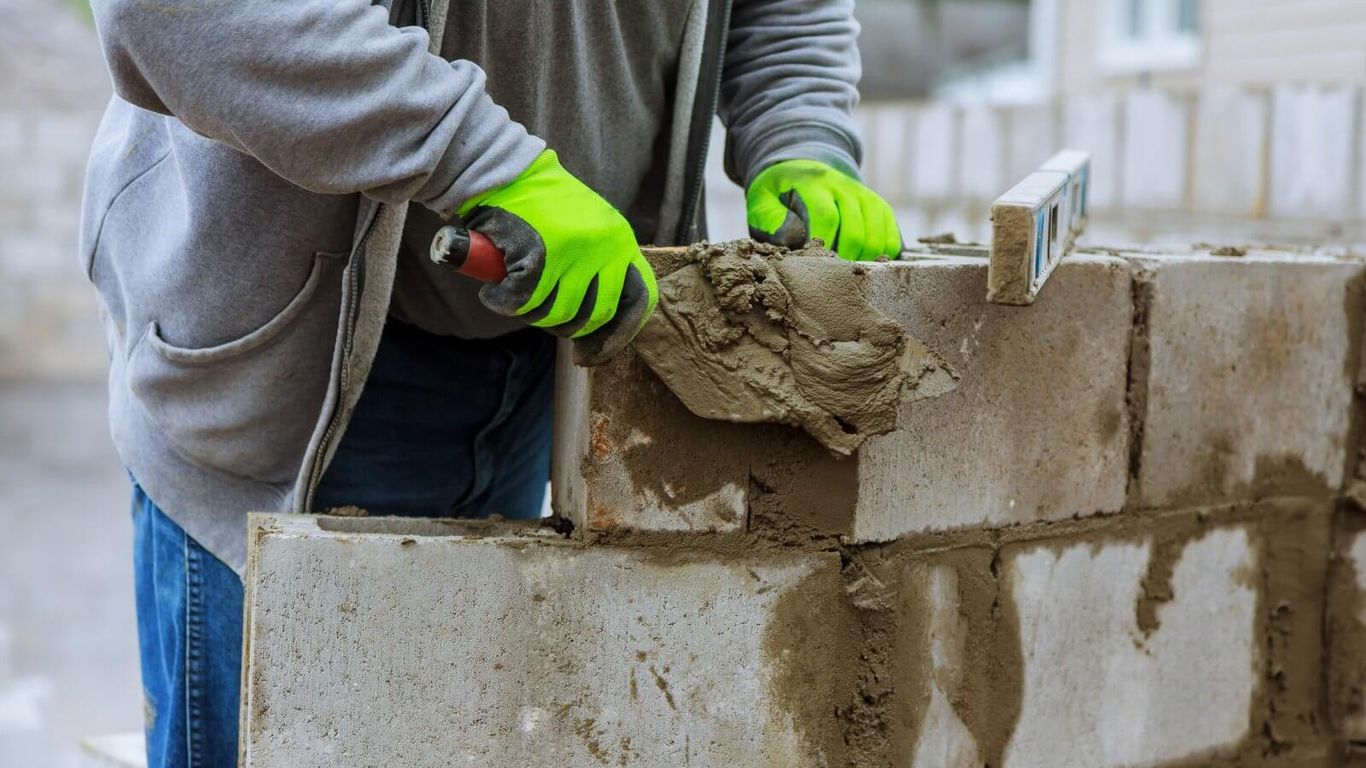 A person is laying concrete blocks with a trowel and level.