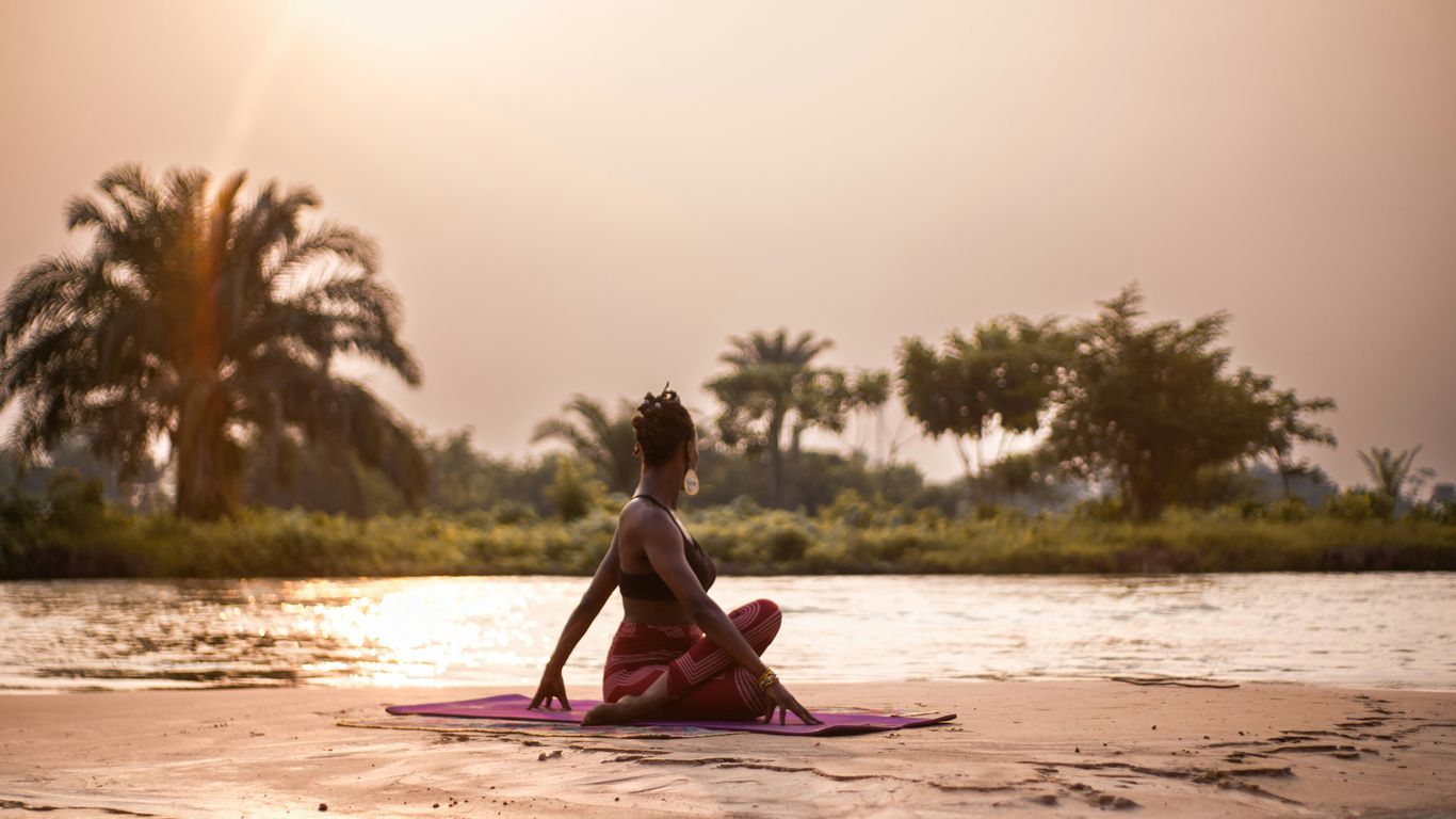 A woman sitting on a pink mat on a river bank