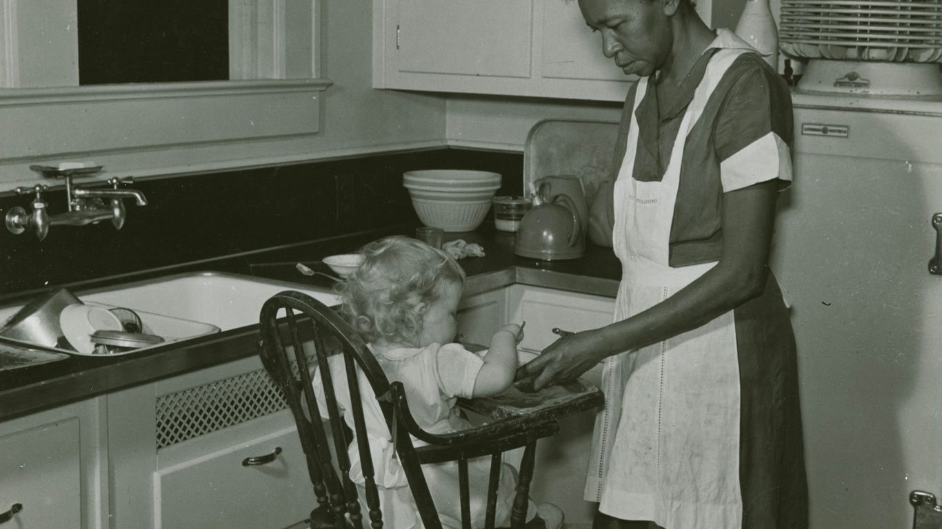 grayscale photography of woman standing in front of baby in highchair