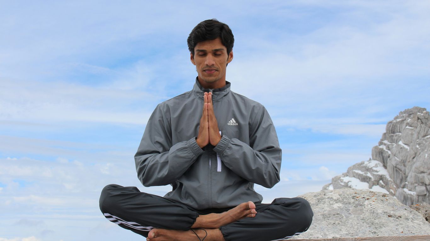 man meditating on brown wooden platform during daytime