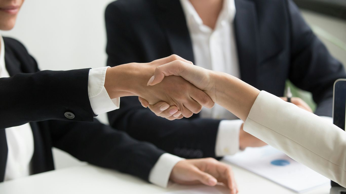 two people shaking hands in front of a laptop