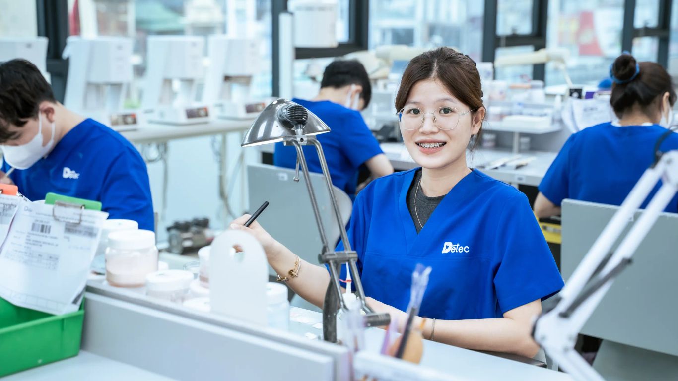 People in blue uniforms working in a dental laboratory.