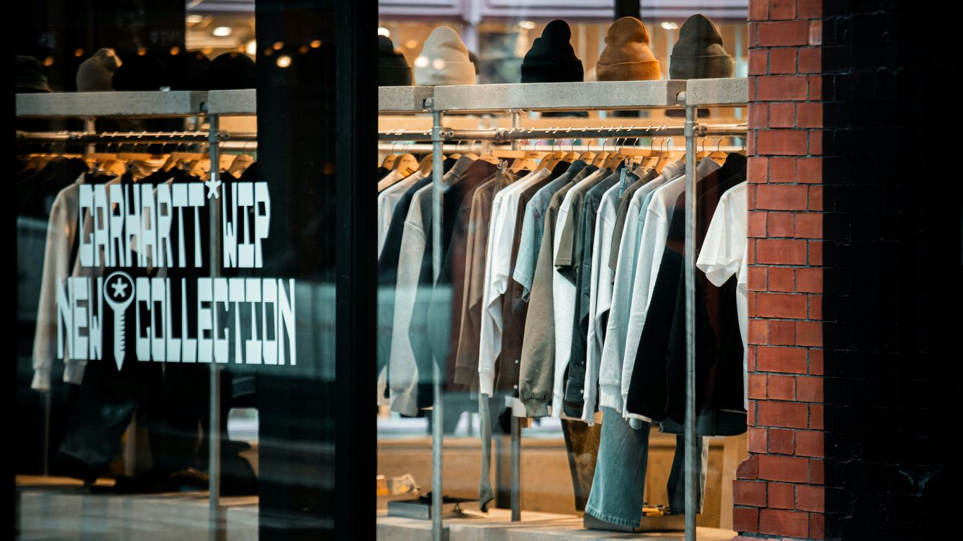 Clothes displayed on racks inside a store window.