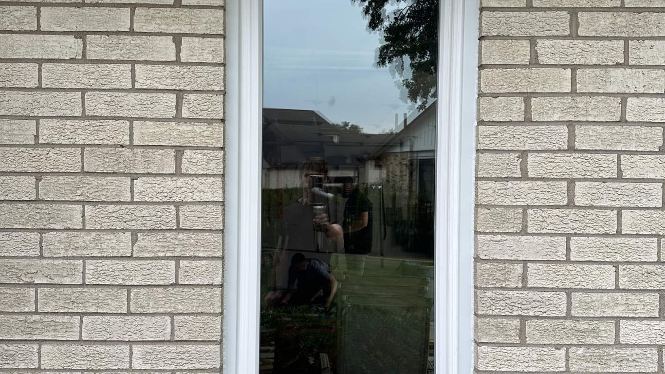 A window reflects a person and a house in a brick wall.