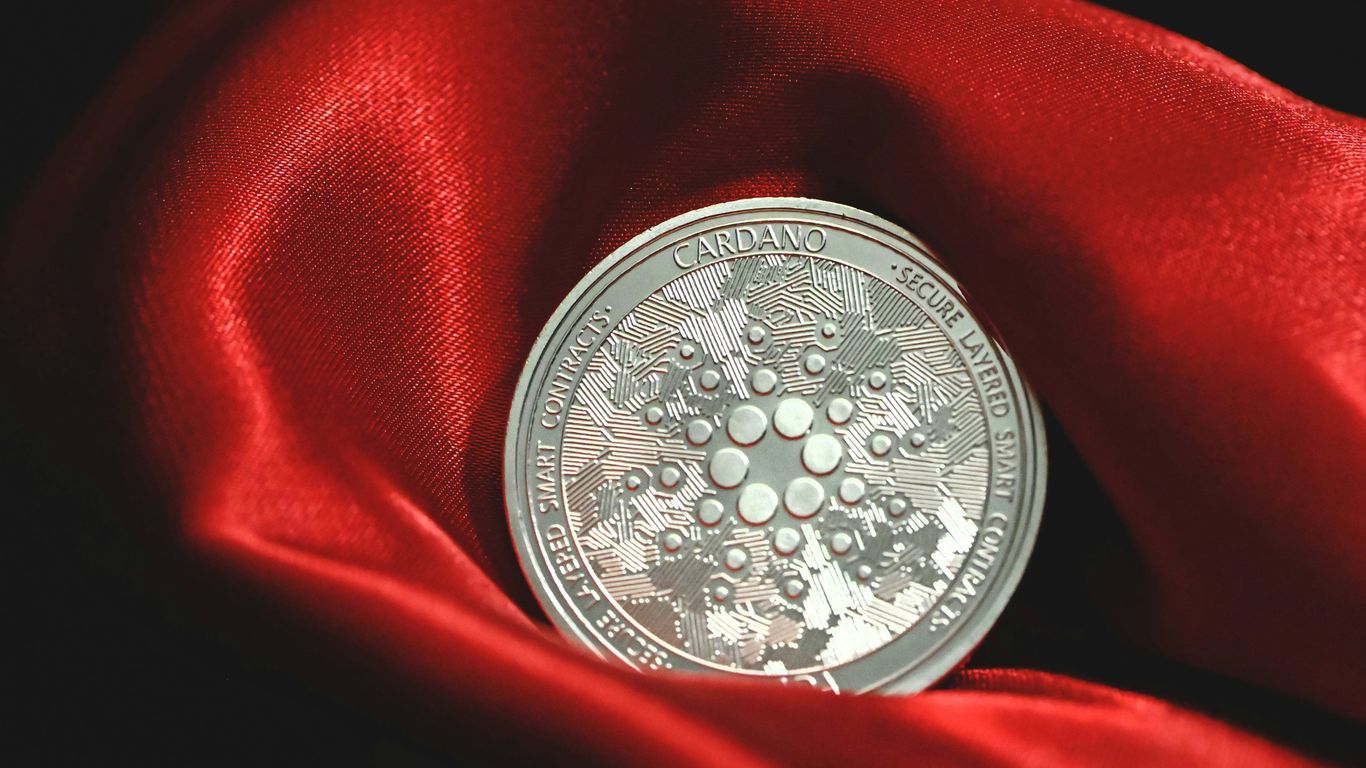 A silver Cardano coin resting on a red satin fabric.