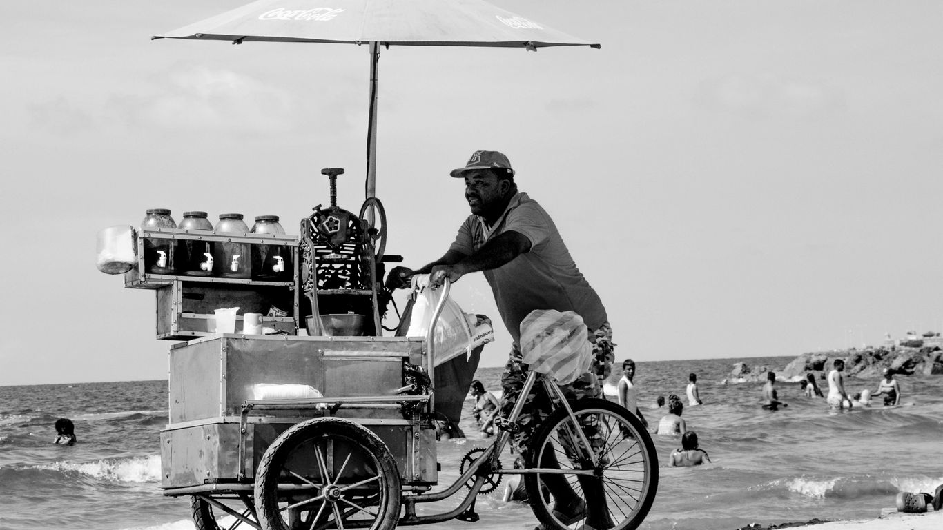 Man pushes a cart with an umbrella on the beach.